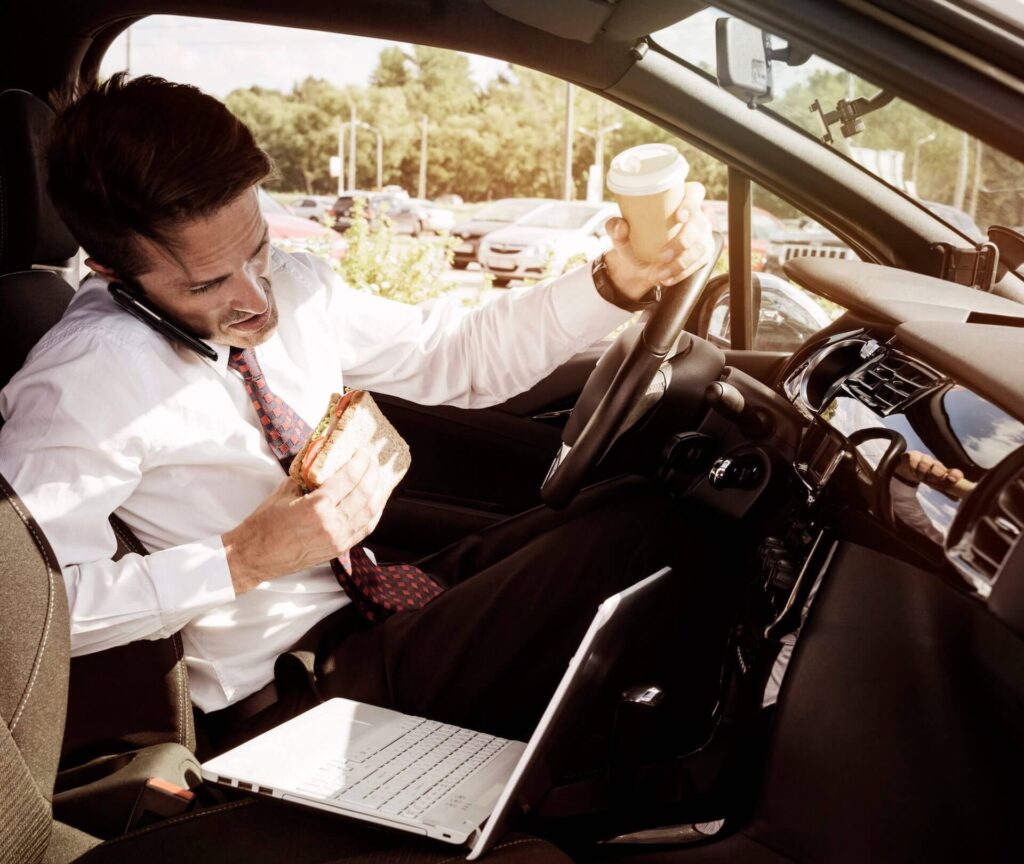 Mann sitzt gestresst im Auto mit ungesundem Fast Food